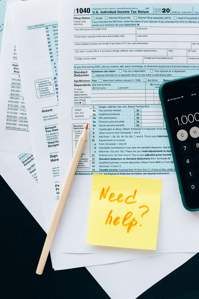 Home Close-up of tax forms with a calculator and a note asking for assistance.