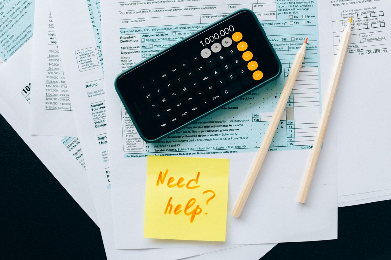 Home Top view of financial papers with a calculator, pencils, and a note saying 'Need help?' indicating tax or accounting assistance.