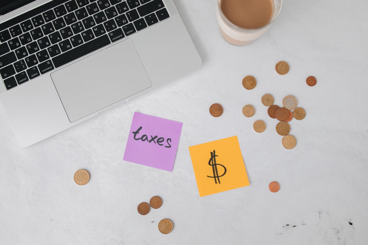 Home A workspace with a laptop, sticky notes, coins, and a coffee cup, ideal for tax planning.