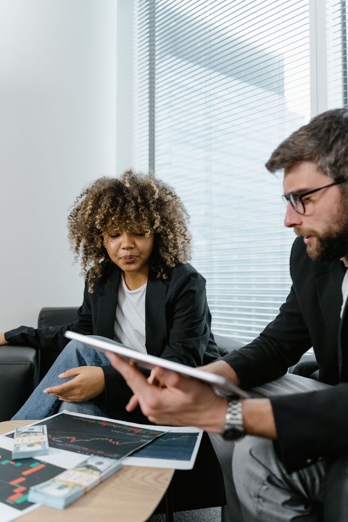 Home Two professionals discussing financial graphs on a tablet in a modern office setting.