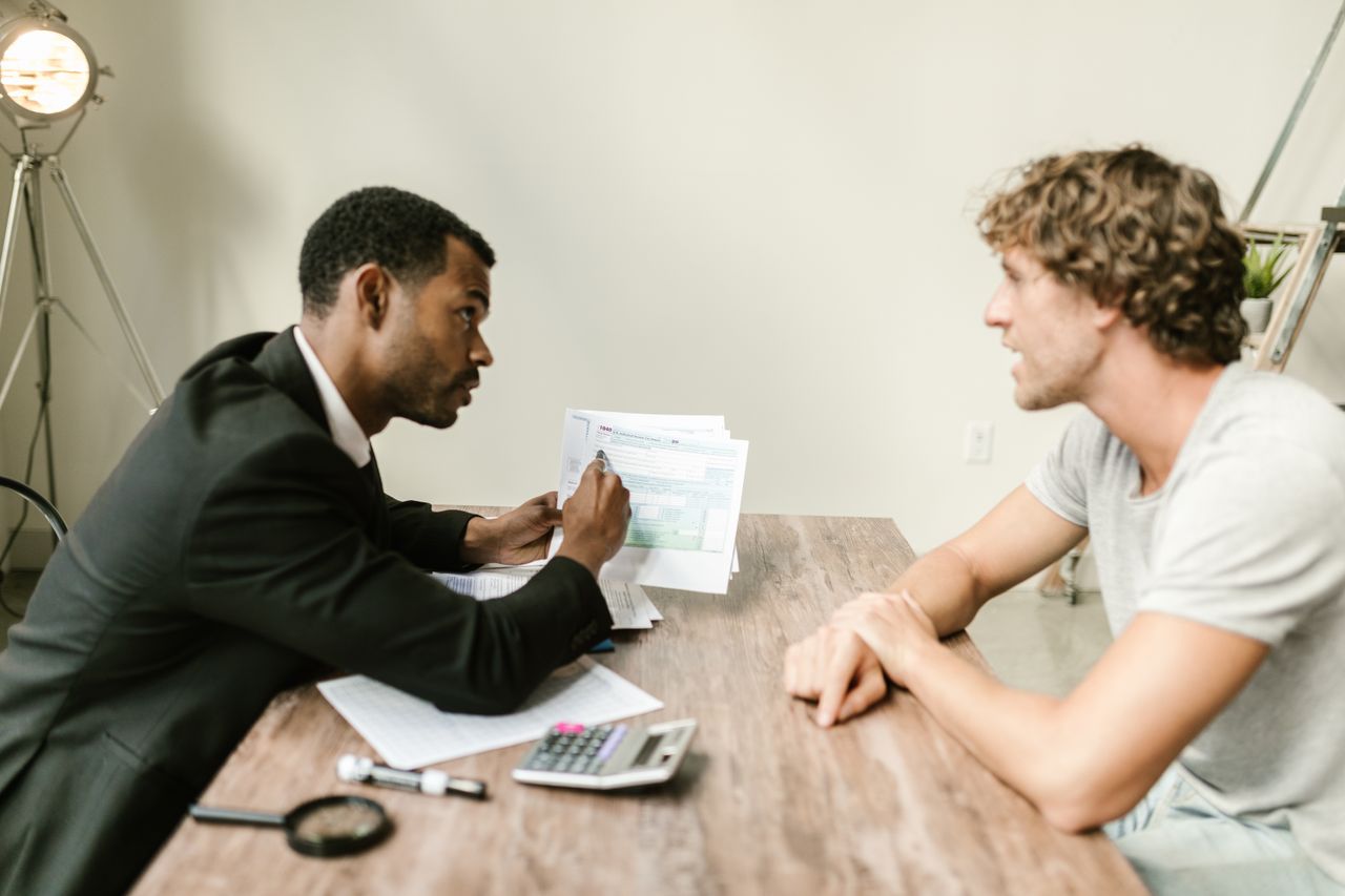 Home A financial advisor discusses paperwork with a client at a desk in a modern office.